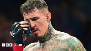 Tom Aspinall dabs his eye after suffering an eye poke during his fight with Cyril Gane at UFC 321