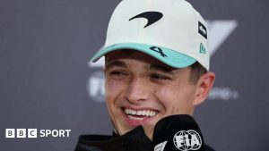 Lando Norris smiles while speaking into an F1 and FIA-branded microphone at a news conference following qualifying for the Sao Paulo Grand Prix