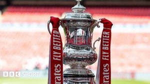 The FA Cup trophy, with red ribbons containing the sponsor