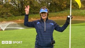 Lyn Parry holds up three fingers and a flag to celebrate her hole-in-one treble success